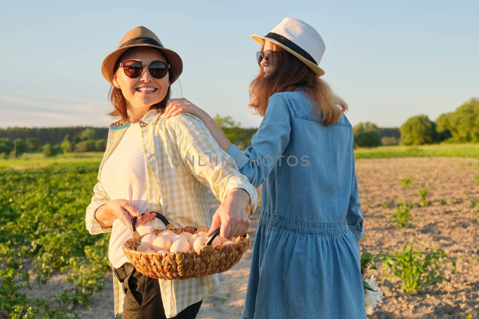 Mother and teen daughter with a basket of fresh eggs in the garden, golden hour by VH-studio