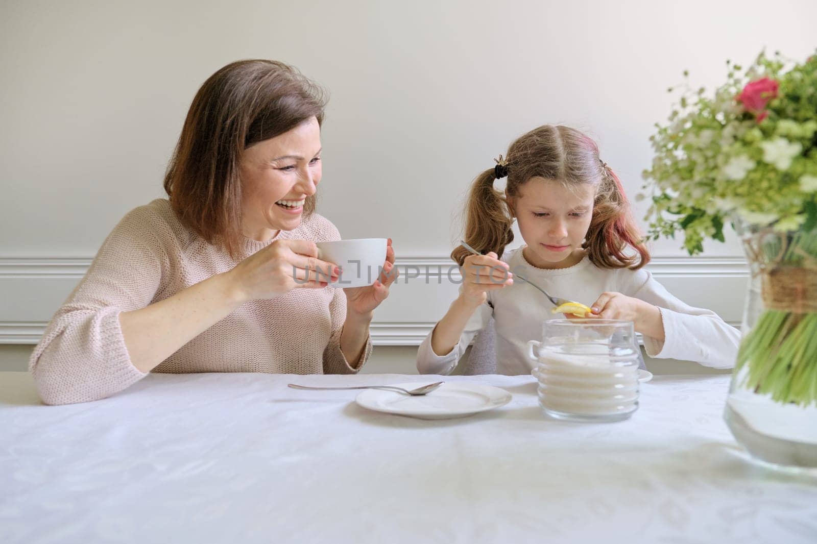 Laughing mother and daughter drinking from cups and eating lemon. by VH-studio