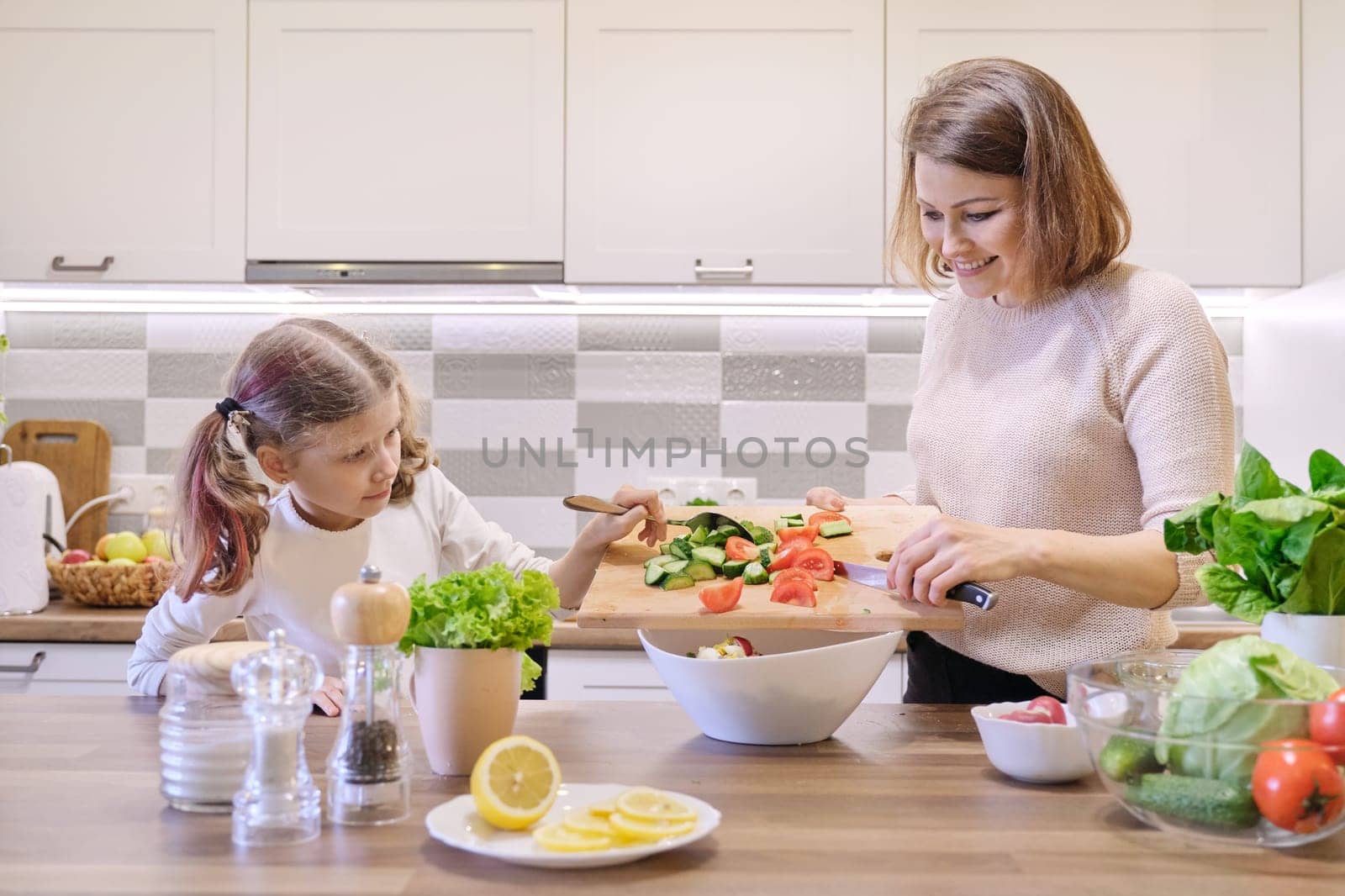 Mother and daughter cooking together in kitchen vegetable salad, parent and child are talking smiling