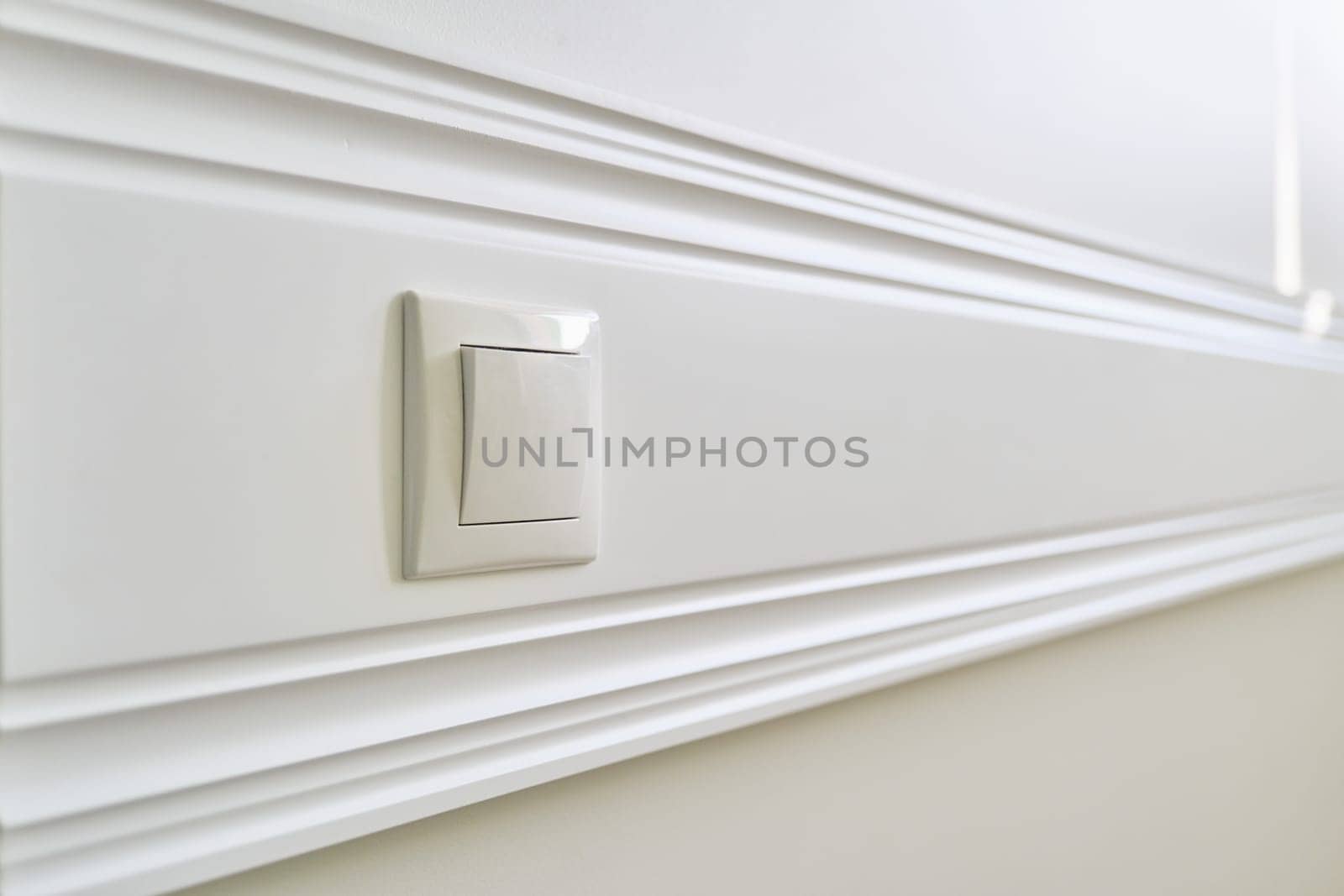 Wooden white painted panel board glued to the wall with power socket in interior close-up by VH-studio