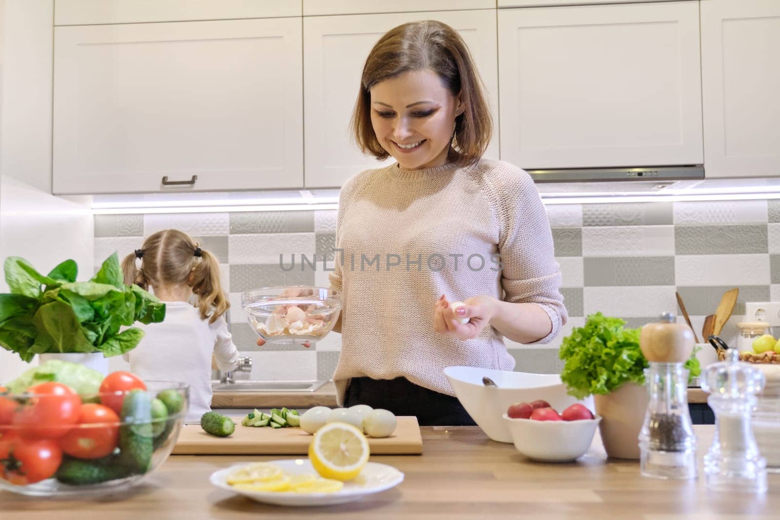 Smiling mother and daughter cooking together in kitchen vegetable salad. by VH-studio