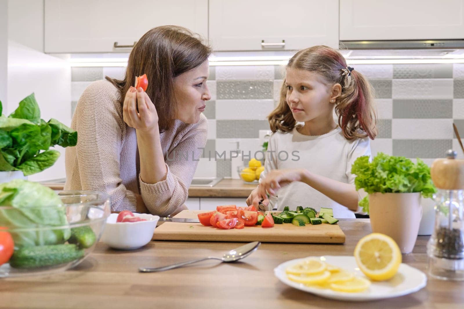 Mother and daughter cooking together in kitchen vegetable salad, parent and child are talking smiling