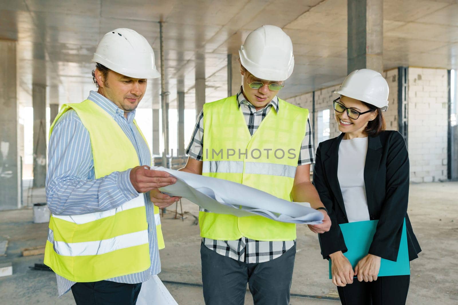 Team of builders engineers at construction site, reading blueprint. by VH-studio