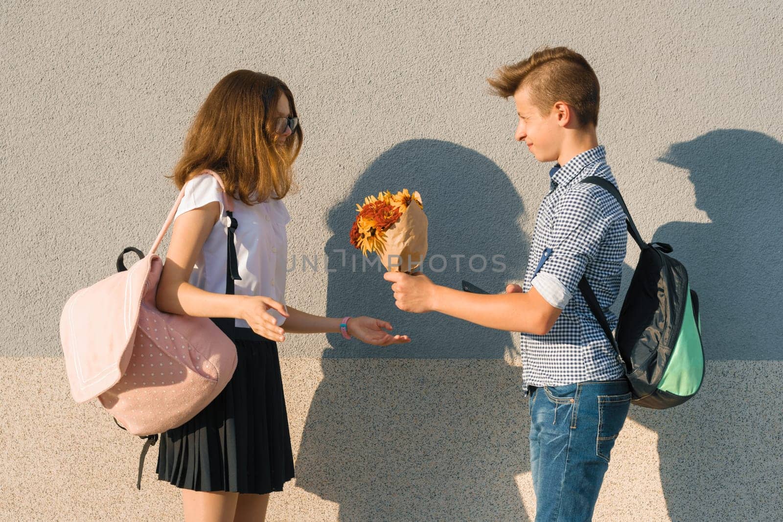 Boy gives girl bouquet of flowers. Outdoor portrait of couple teenagers by VH-studio