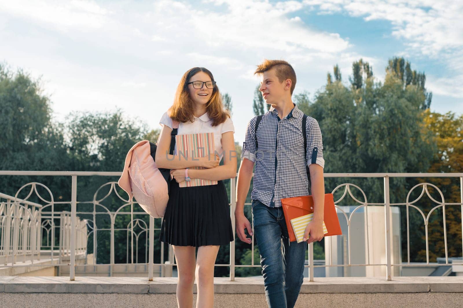 Adolescents students with backpacks, textbooks, go to school. Outdoor portrait of teenage boy and girl 14, 15 years old.