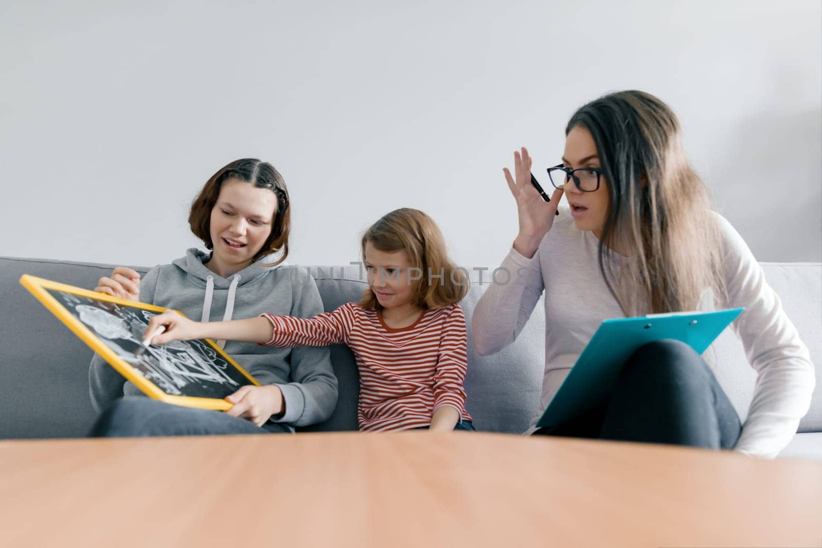 Two sister girls talking with young woman family psychologist, children sitting in office by VH-studio