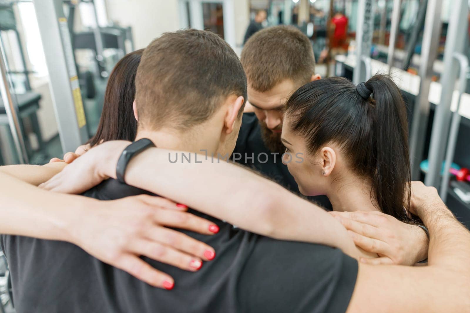 Group of young sports people embracing together in fitness gym backs. Fitness, sport, teamwork, motivation, people, healthy lifestyle concept.