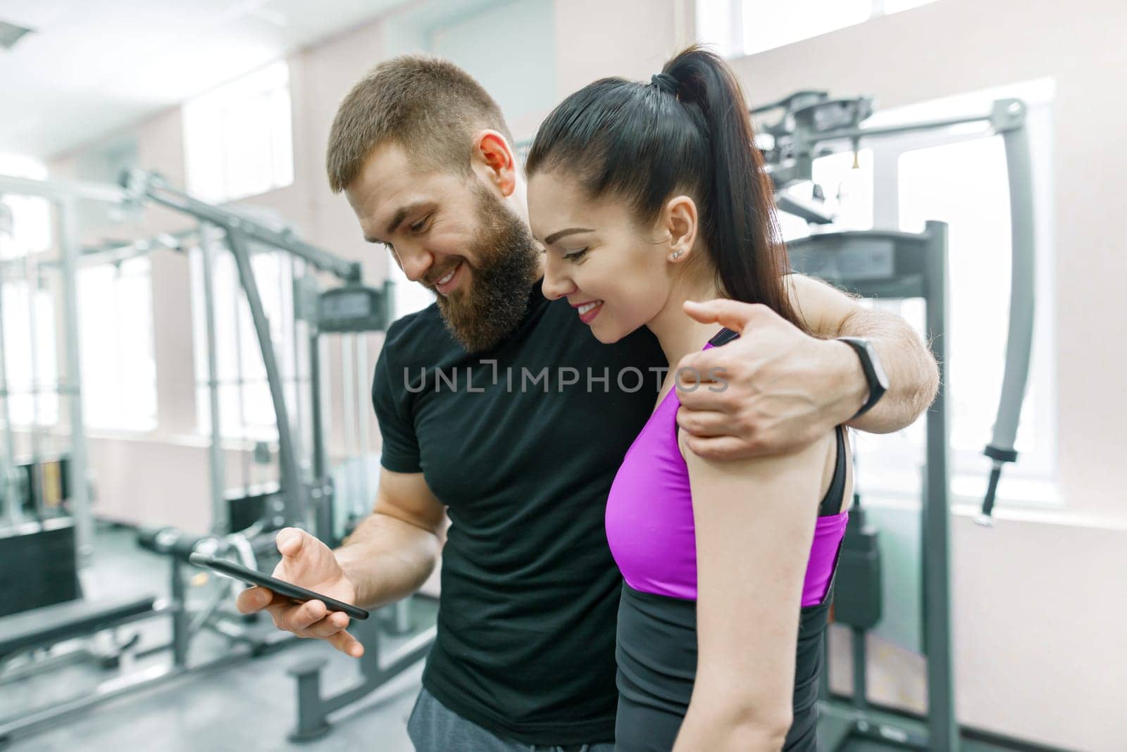 Young woman talking with personal trainer in gym, looking in smartphone and discussing. Fitness, sport, training, people, healthy lifestyle concept.