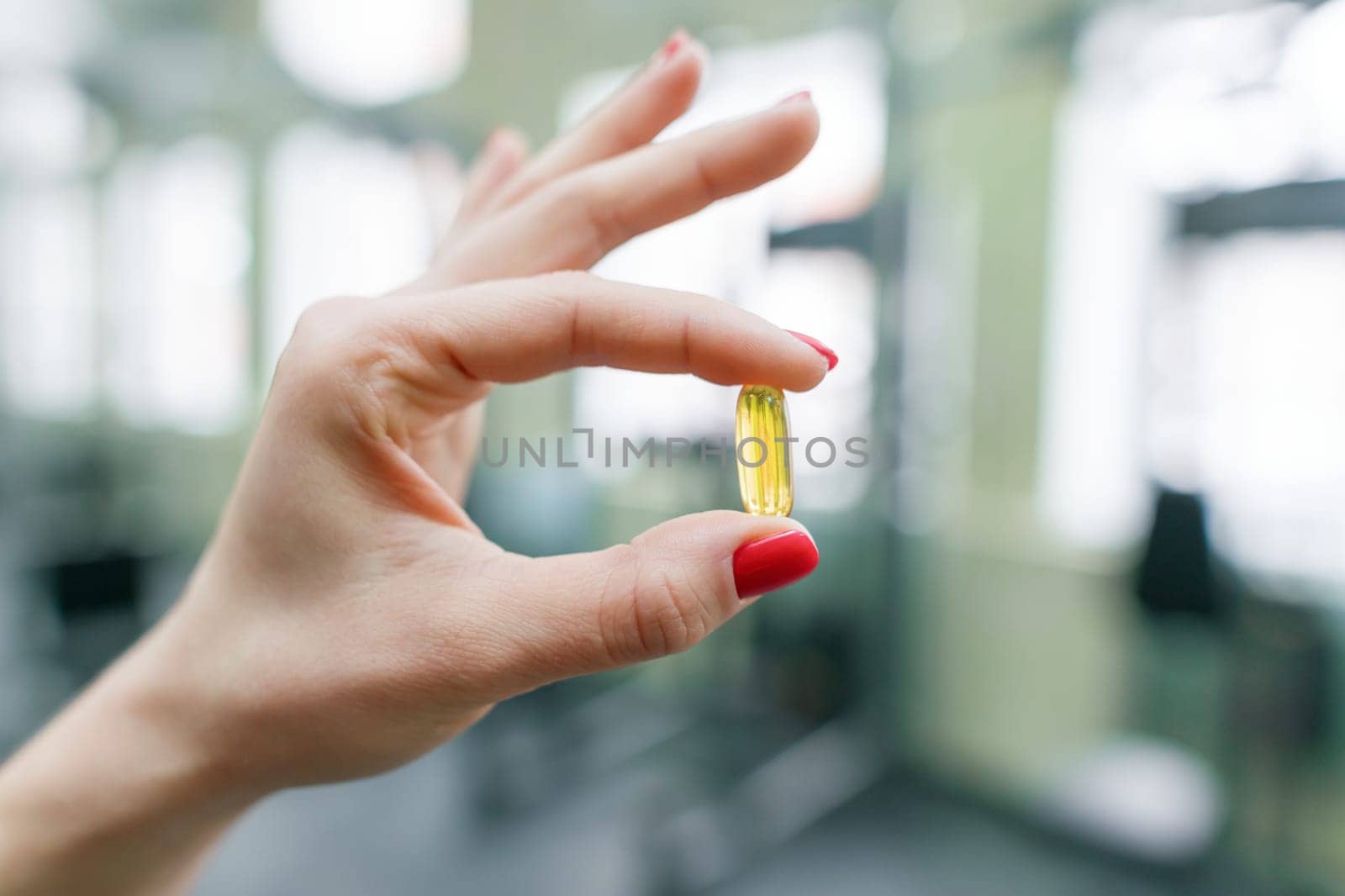 Closeup of fitness woman hands showing vitamin e capsule omega-3, gym background. Healthy lifestyle, medicine, nutritional supplements and people concept.