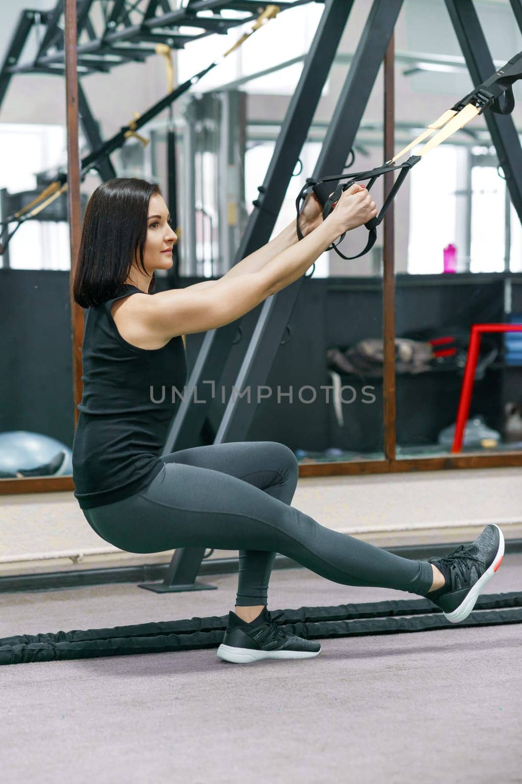 Portrait of young athletic woman training with fitness loop system in gym. by VH-studio