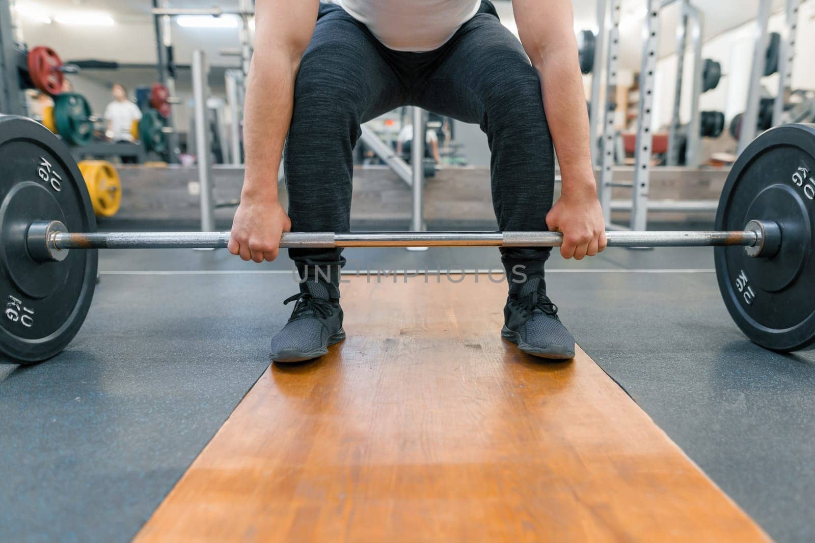 Closeup of arms and legs of man exercising with barbell at sport gym. Athlete, bodybuilding, training, weightlifting, workout exercises concept.