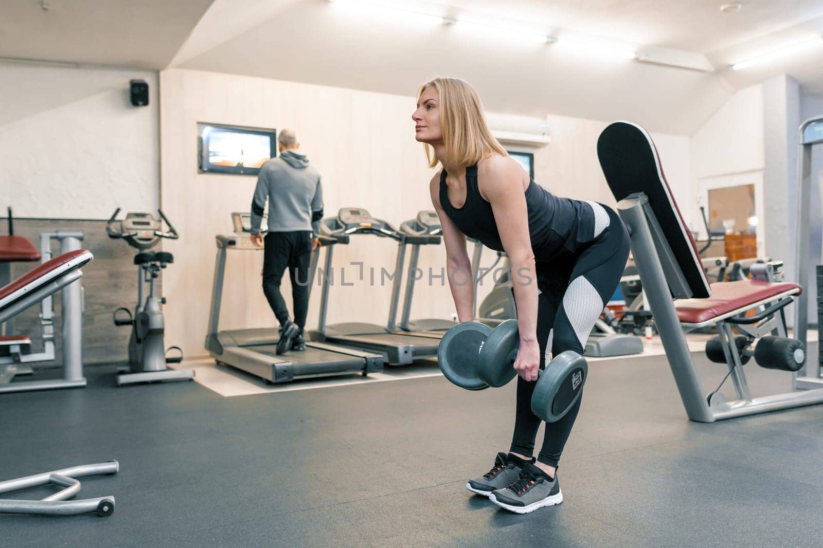 Young beautiful blond woman doing strength exercises with dumbbells in gym. Sport, fitness, bodybuilding, training, workout exercises concept.