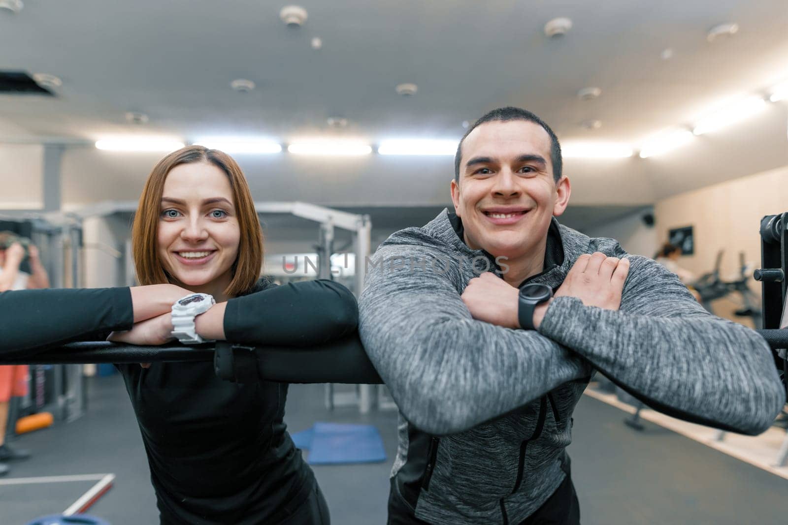 Portrait of young happy sporty couple, man and woman smiling looking into the camera, gym background by VH-studio