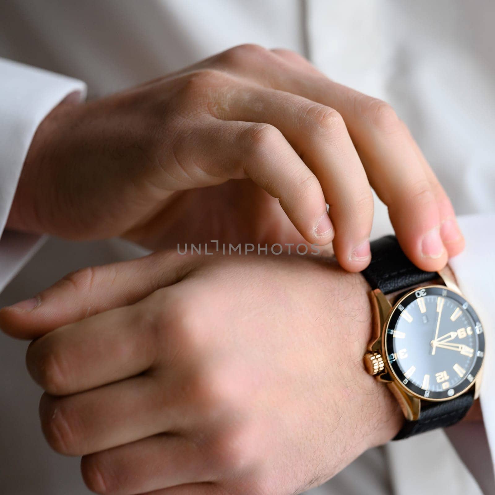 The morning of the groom on the wedding day before the wedding ceremony, the man adjusts the clock on his hand.