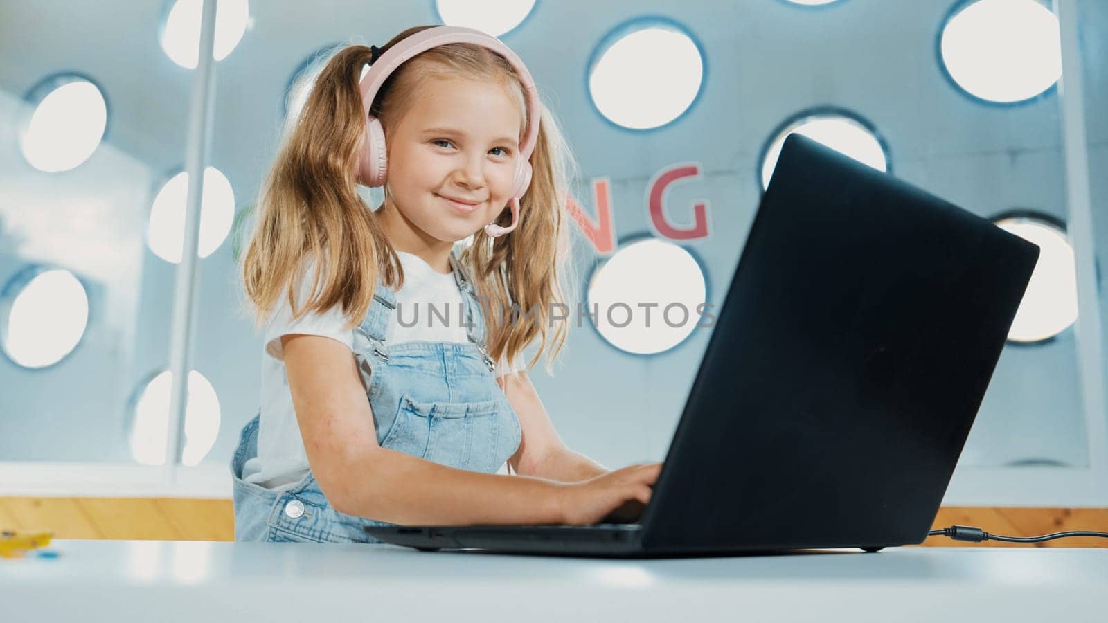 Young student working on laptop or studying in online classroom. Caucasian girl typing on laptop while doing homework or listening music.Little kid wearing headphone. Creative learning. Erudition.