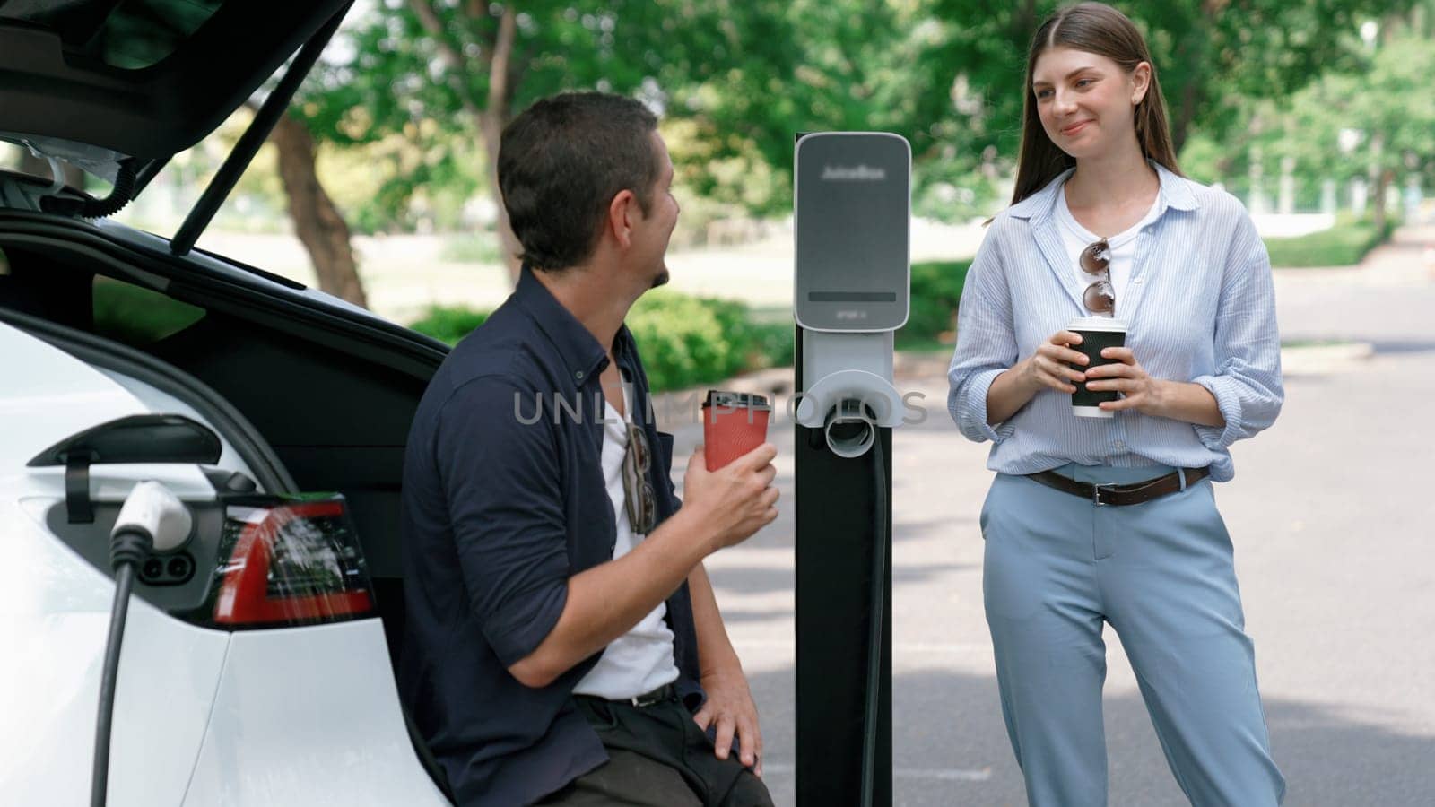 EV car recharging electricity for battery by lovey couple on road trip. Exalt by biancoblue