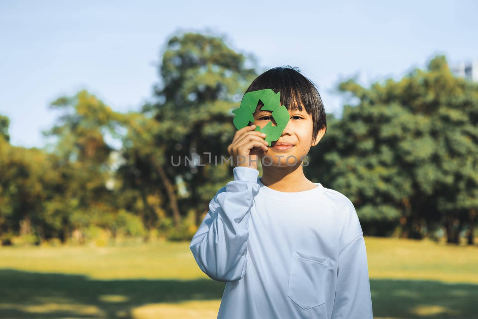 Cheerful young asian boy holding recycle symbol on daylight natural green park promoting waste recycle, reduce, and reuse encouragement for eco sustainable awareness for future generation. Gyre