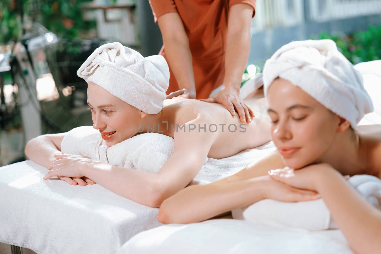 Couple of beautiful young woman lie on white spa bed during having back massage. Attractive caucasian woman having back massage at traditional spa room. Relaxing and healthy concept Tranquility.