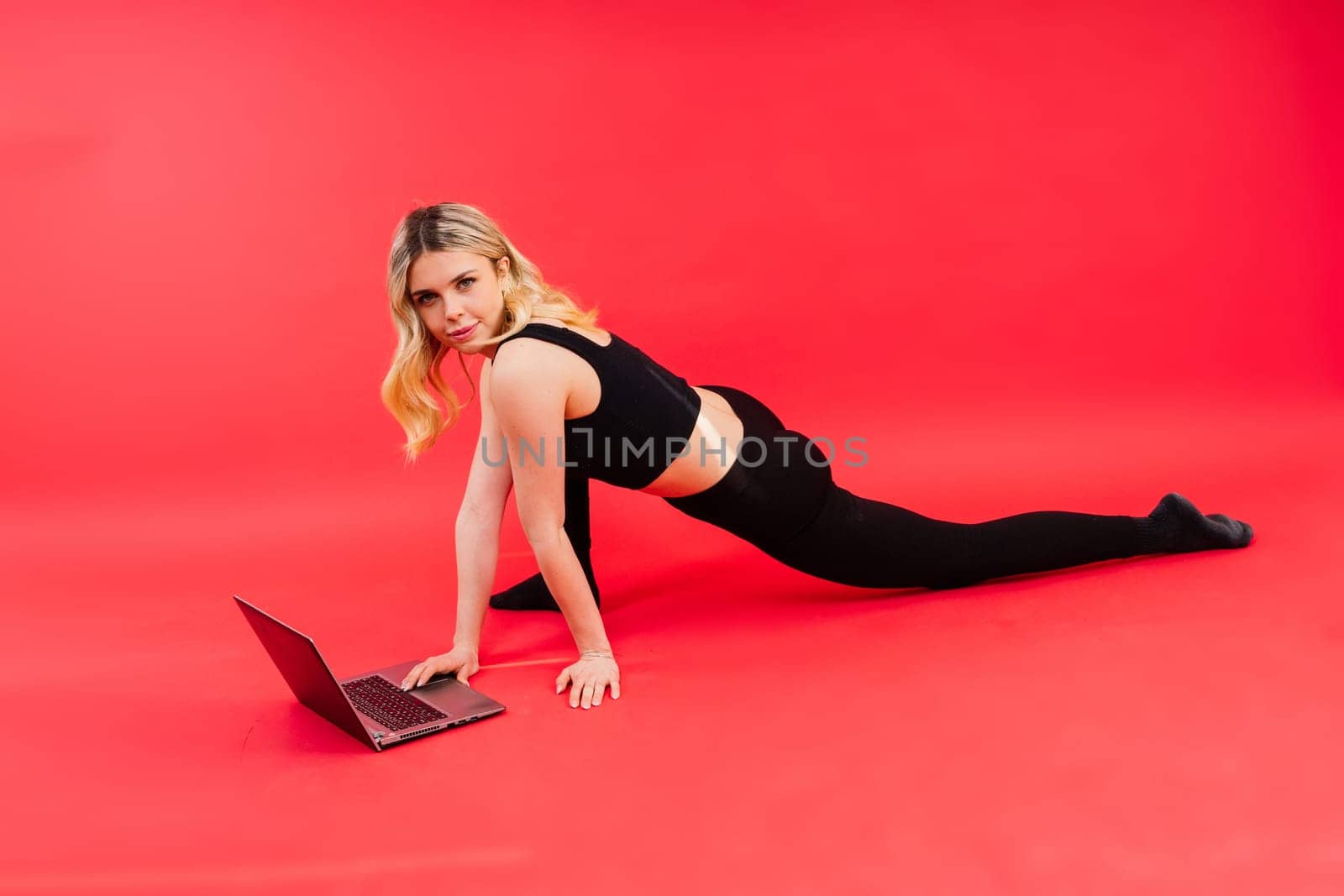 Fit woman doing stretching exercise and watching meditation video on a laptop in studio.
