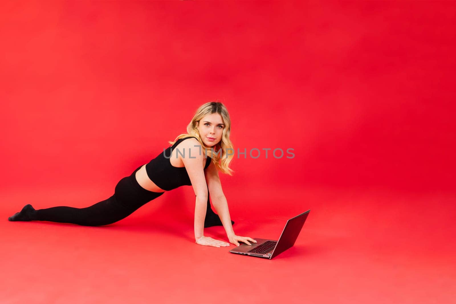 Fit woman doing stretching exercise and watching meditation video on a laptop in studio.