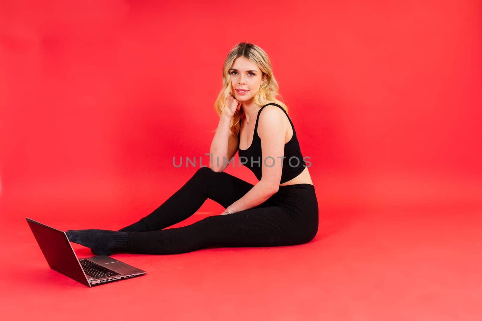 Fit woman doing stretching exercise and watching meditation video on a laptop in studio.