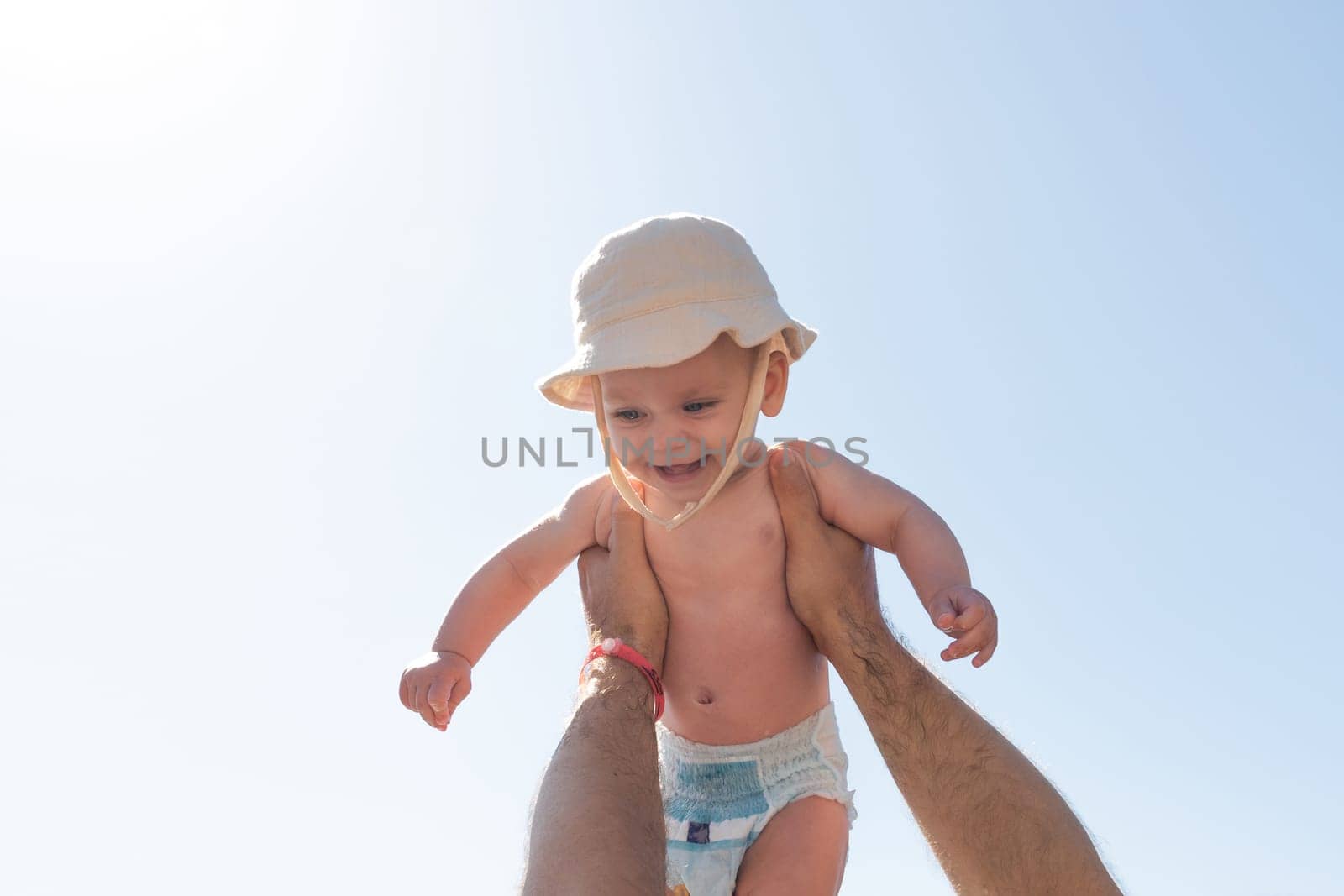 In a sun-kissed setting, a father joyfully lifts his baby towards the sky, capturing the essence of love and play. Concept of family bonding and joyful childhood