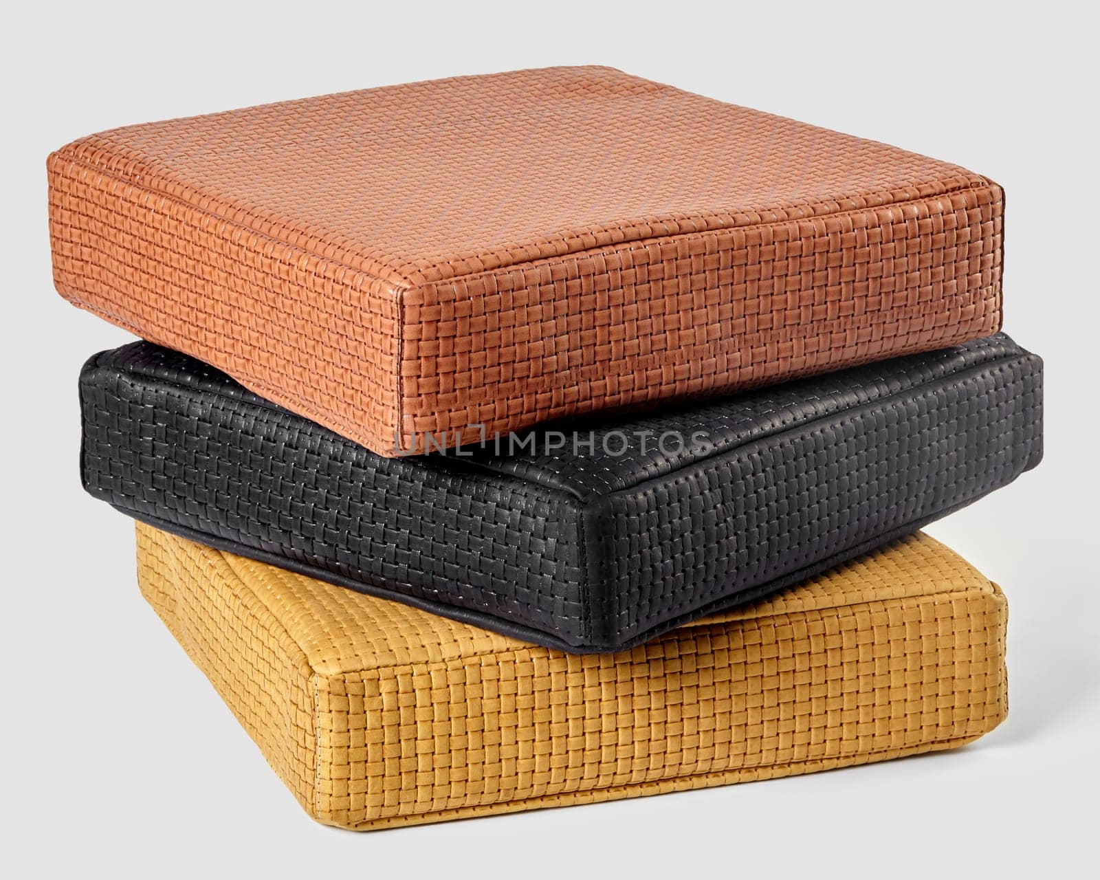 Elegantly stacked leather cushions with woven texture in shades of tan, black, and yellow. Artisanal accessories offering comfort and sophistication to interior
