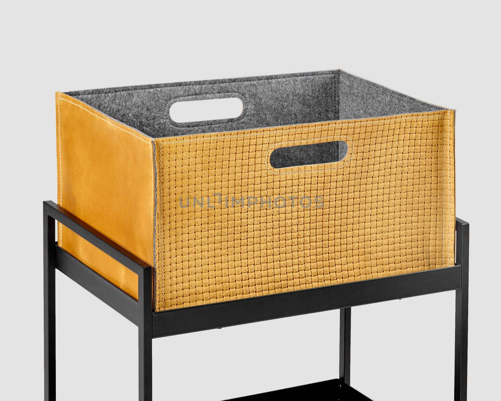 Comfortable tan suede woven box with convenient slotted handles for storing office supplies and document placed on metal shelving rack. Stylish craft accessory for interior design