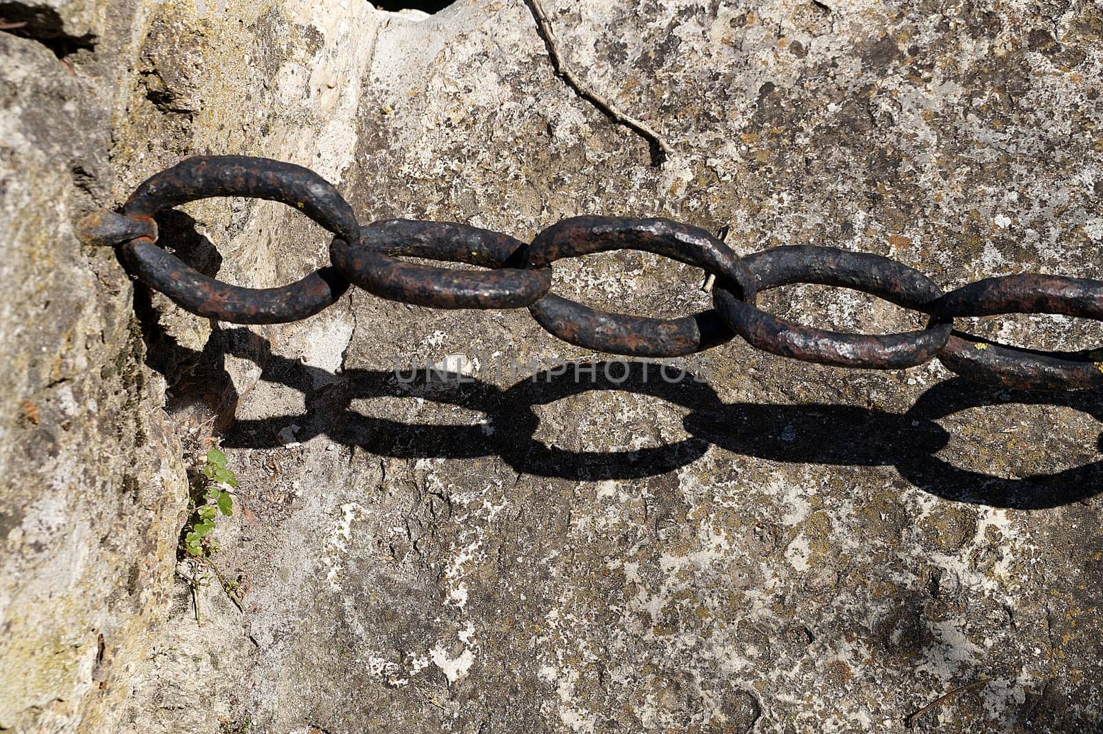 vintage wrought iron chain on old stone wall by Annado