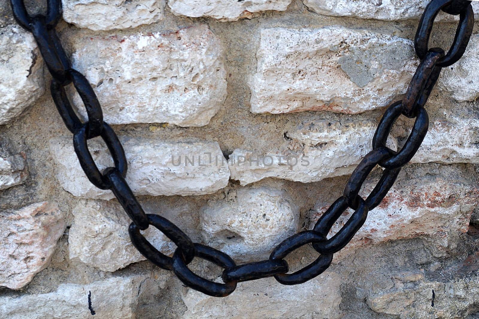 vintage metal chain on an ancient stone wall by Annado