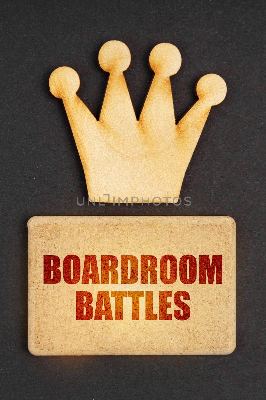 Business concept. On a black background there is a wooden crown of the leader and a sign with the inscription - Boardroom Battles