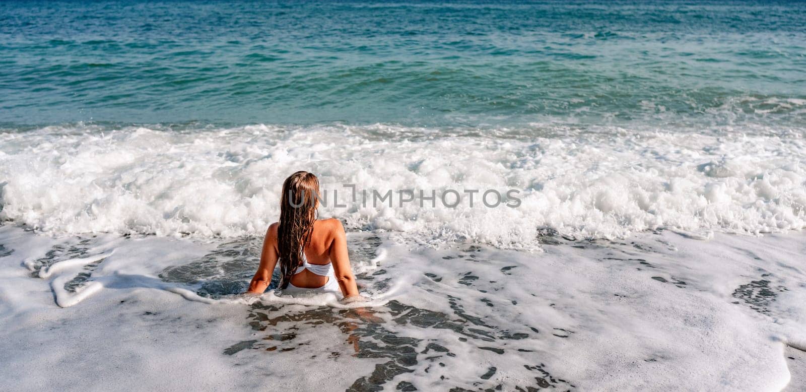 Happy woman in bikini sits on the sea beach. Tanned girl sunbathing on a beautiful shore. Summer vacation or holiday travel concept.