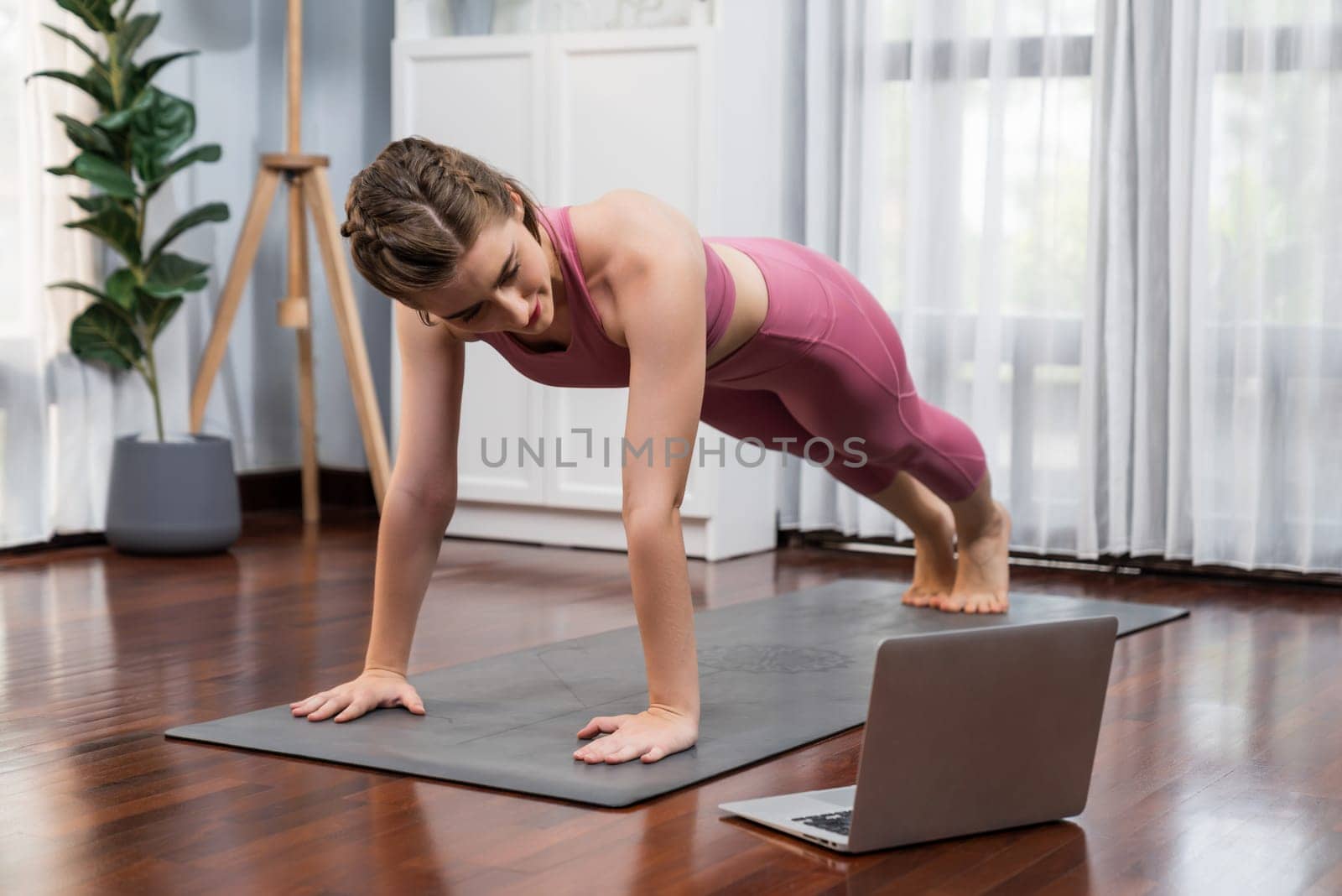 Flexible and dexterity woman in sportswear doing yoga position in meditation posture on exercising mat at home. Healthy gaiety home yoga online training session with peaceful mind and serenity.