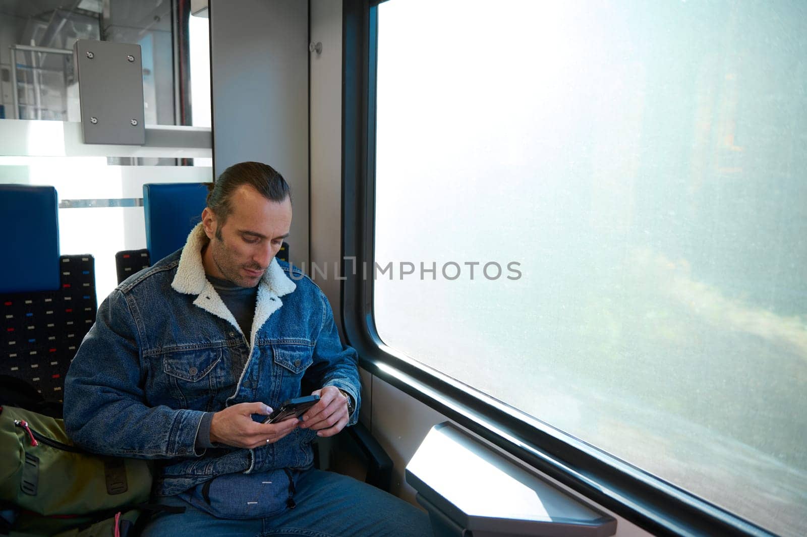 Caucasian man commuter using smartphone, checking mobile app, planning route while travelling by comfortable city train. by artgf