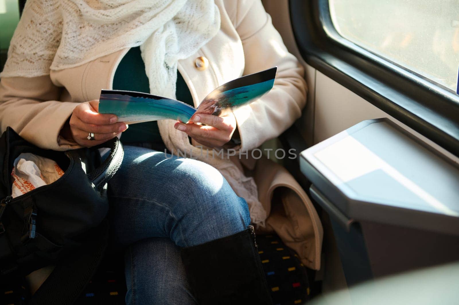 Close-up a leaflet in hands of a female commuter riding on a high speed train. people. Leisure. Rail road transportation by artgf