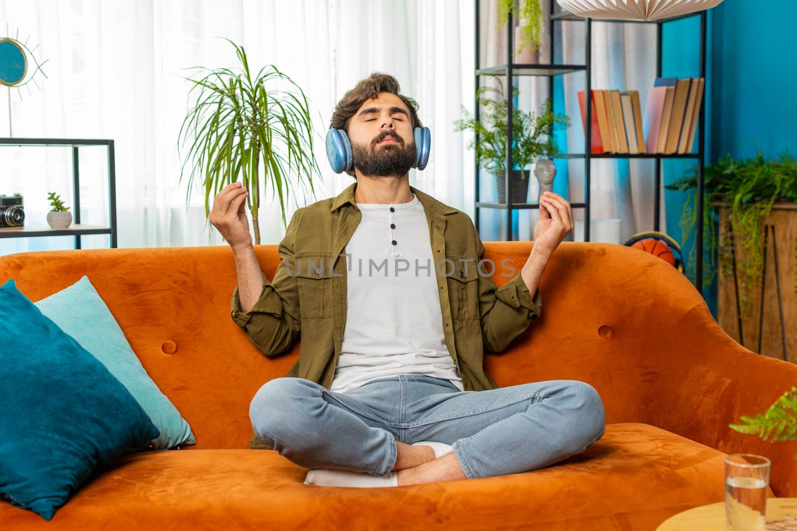 Keep calm down, relax. Middle eastern arabian man listening music breathes deeply, eyes closed meditating with concentrated thoughts, peaceful mind. Young bearded guy sits at home in room on couch