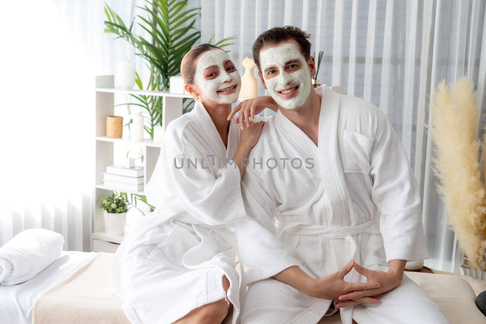 Blissful couple in bathrobe with facial cream mask enjoying serene ambiance of spa salon resort or hotel during holiday. Pampering face spa and skincare treatment with essence relaxation. Quiescent