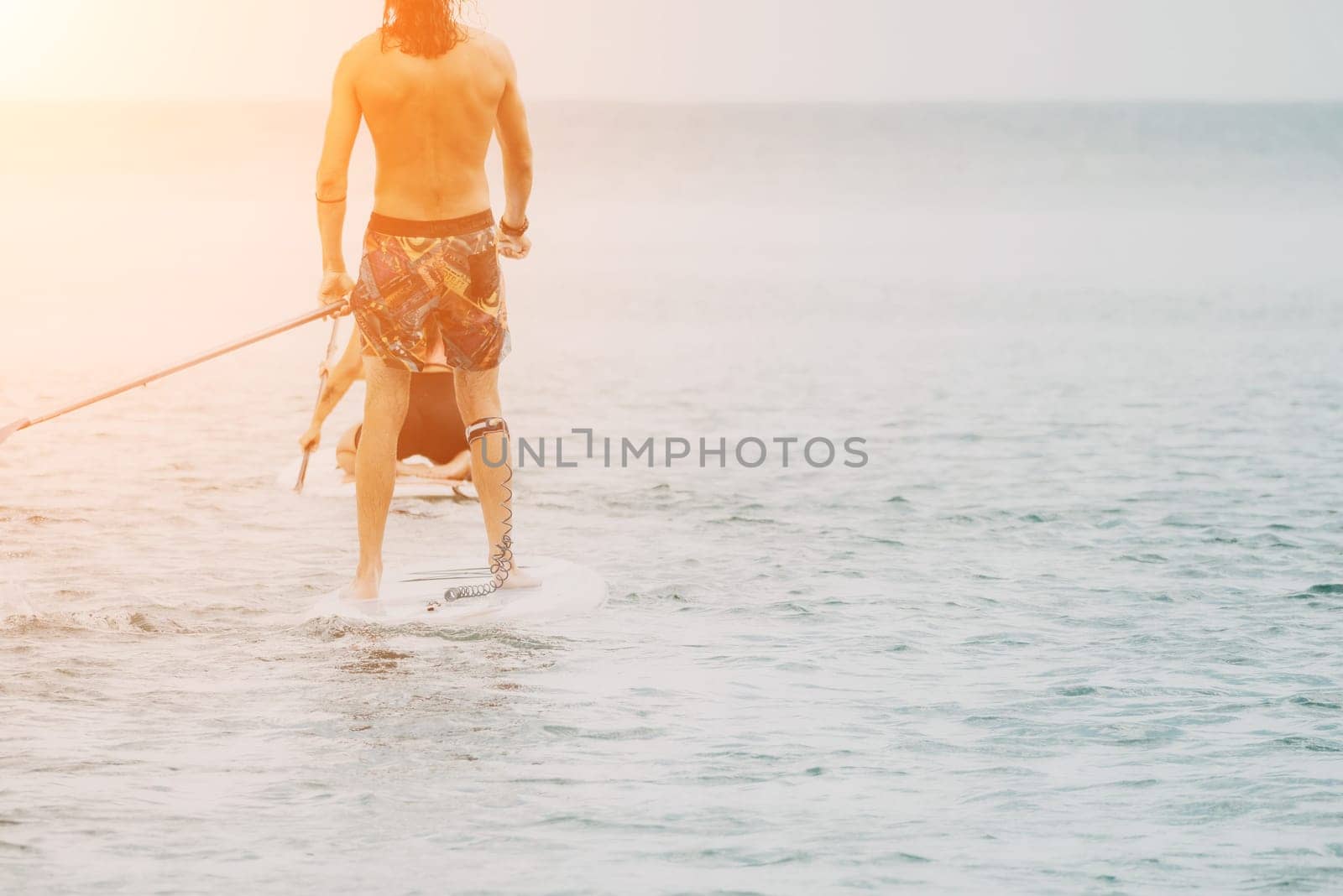 Sea woman and man on sup. Silhouette of happy young woman and man, surfing on SUP board, confident paddling through water surface. Idyllic sunset. Active lifestyle at sea or river