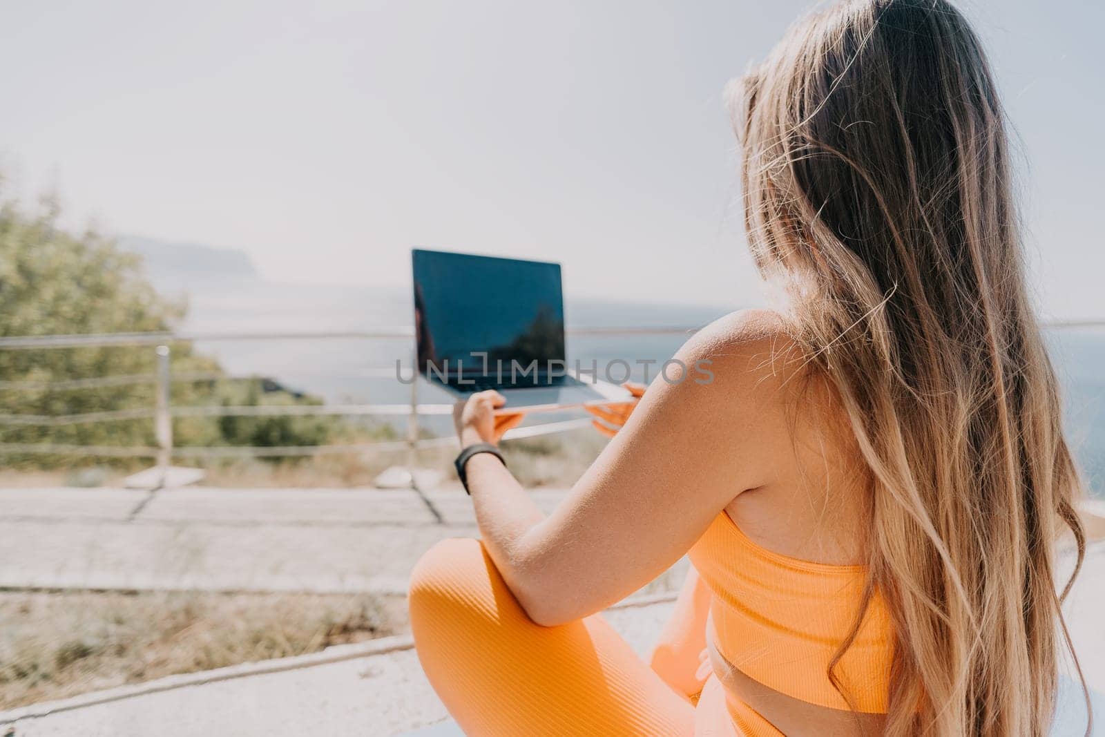 Digital nomad, Business woman working on laptop by the sea. Pretty lady typing on computer by the sea at sunset, makes a business transaction online from a distance. Freelance, remote work on vacation