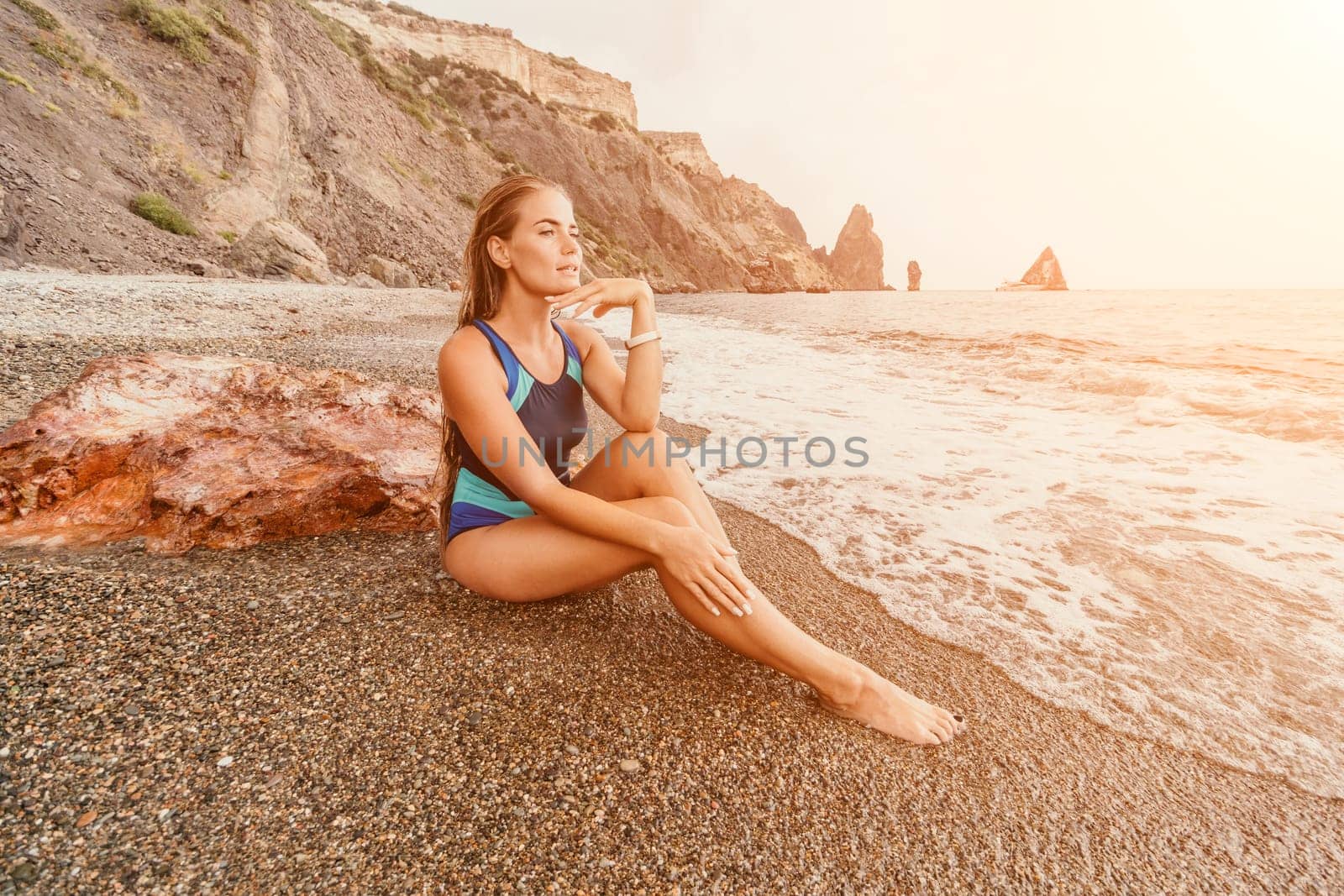 Woman summer travel sea. Happy tourist in blue bikini enjoy taking picture outdoors for memories. Woman traveler posing on the beach surrounded by volcanic mountains, sharing travel adventure journey by panophotograph