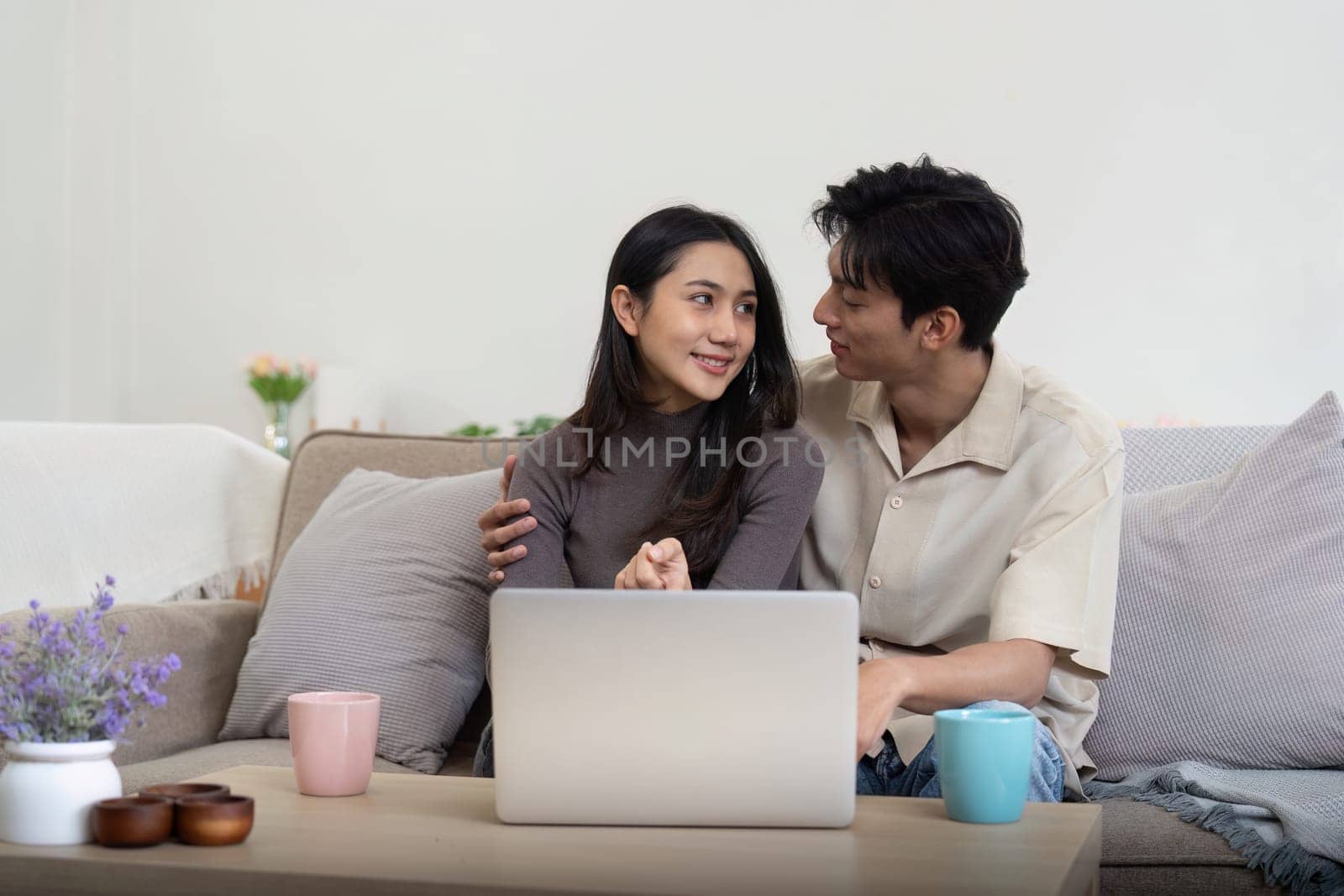 Young couple asian using laptop together while sitting on sofa at home by nateemee