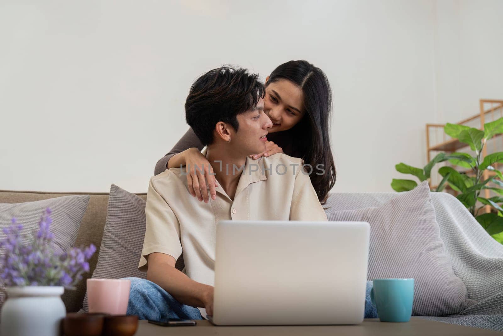 Young couple asian using laptop together while sitting on sofa at home.