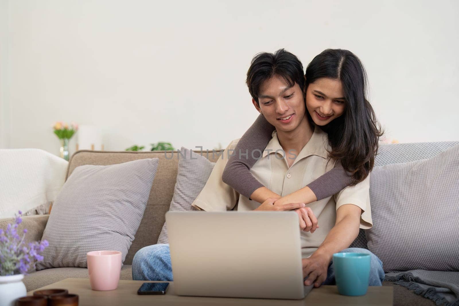 Young couple asian using laptop together while sitting on sofa at home by nateemee