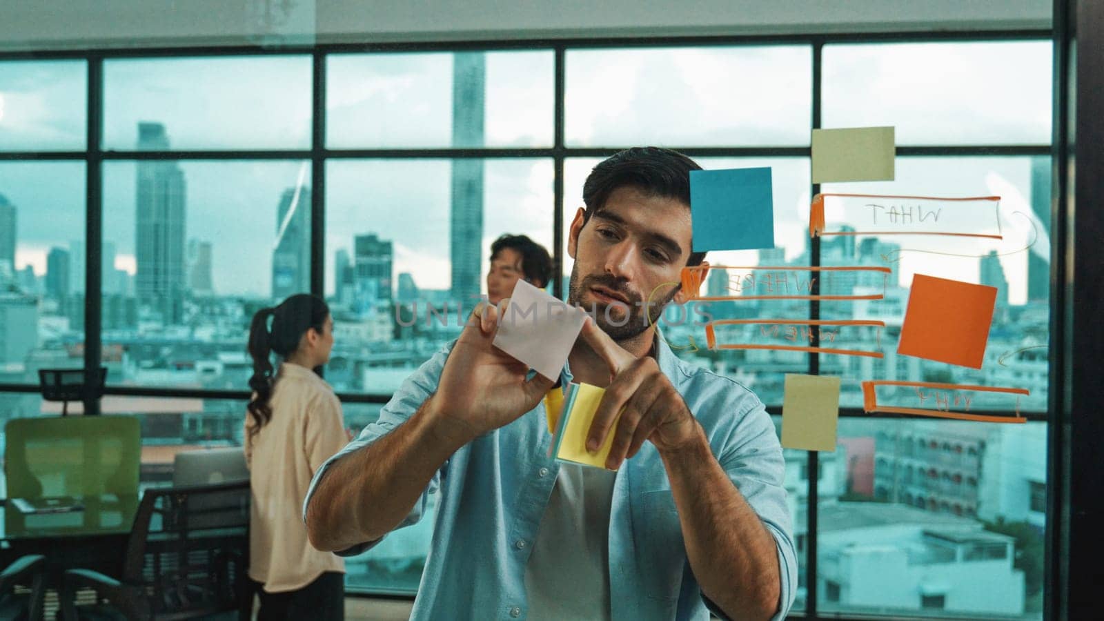 Smart project manager writing sticky notes and mind mapping at glass wall to planing strategy while multicultural businesspeople discussing about business plans at office with city view. Tracery