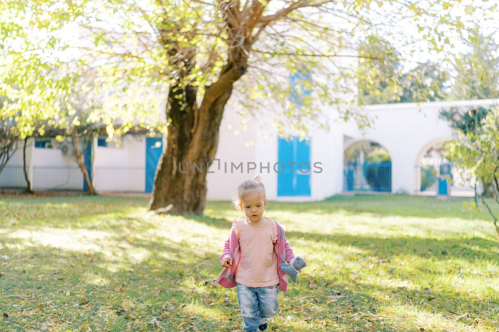 Little girl with a soft toy in her hand walks in a green garden. High quality photo