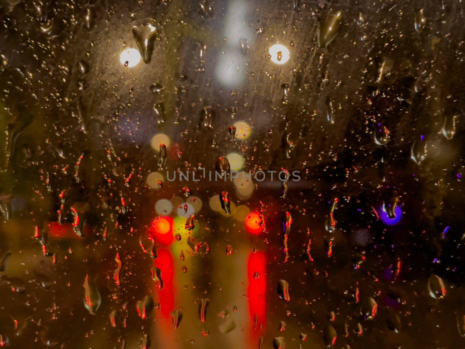 Rain bokeh road lights. Abstract shot of evening city traffic bokeh. Multicolored lights of the evening city and passing cars through a wet rainy window