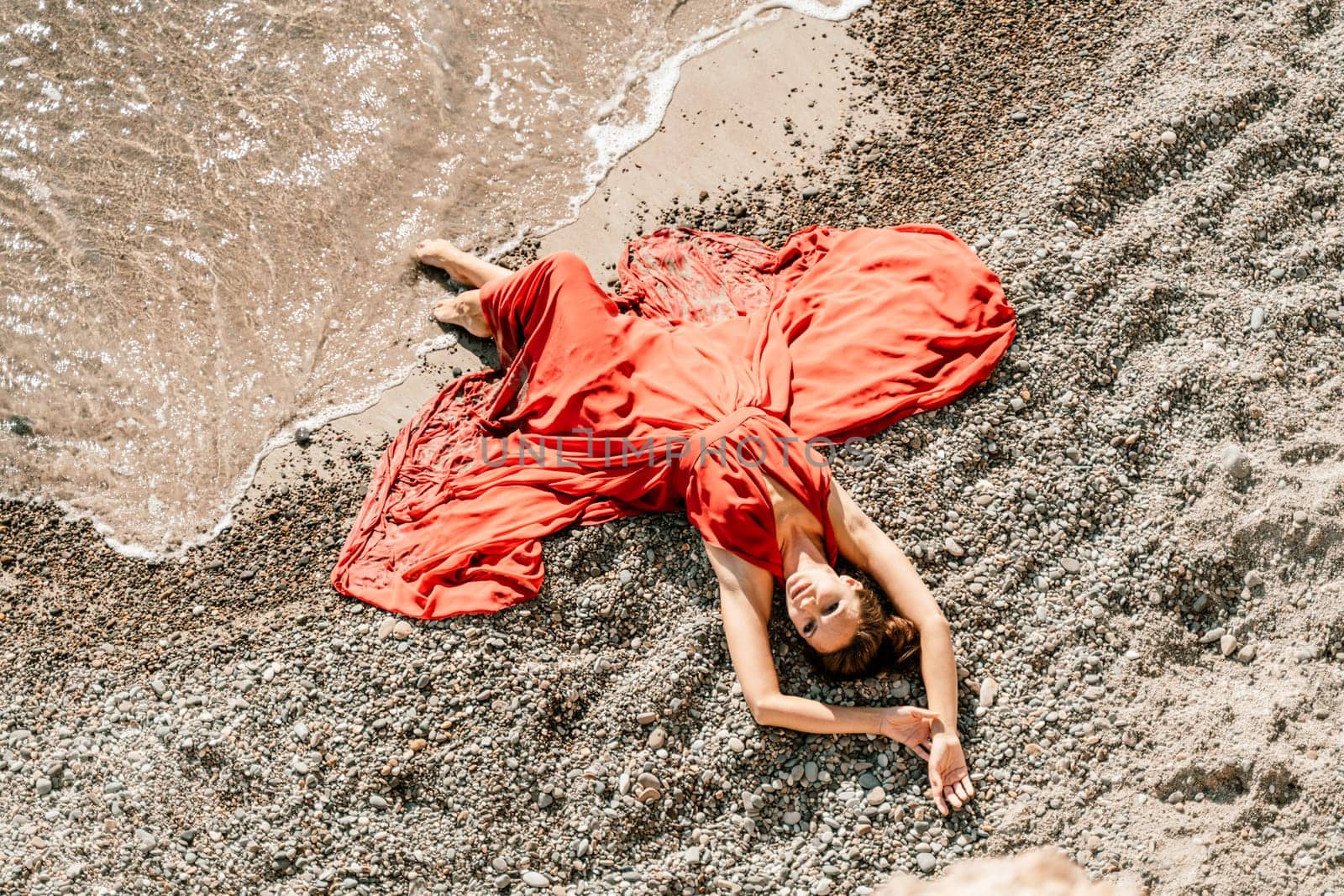 Woman red dress sea. Female dancer in a long red dress posing on a beach with rocks on sunny day by Matiunina