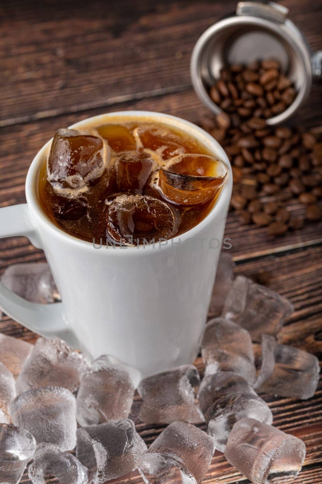 A cup of Iced Americano Coffee with ice cubes placed on a wooden table in a coffee shop by Sonat