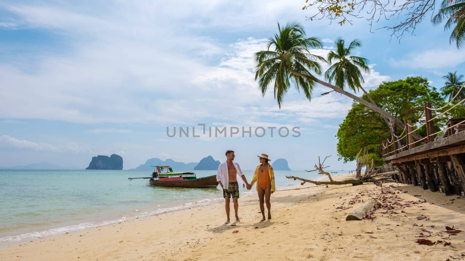 a couple of European men and an Asian Thai woman walking on the beach of the tropical island Koh Ngai Trang Thailand