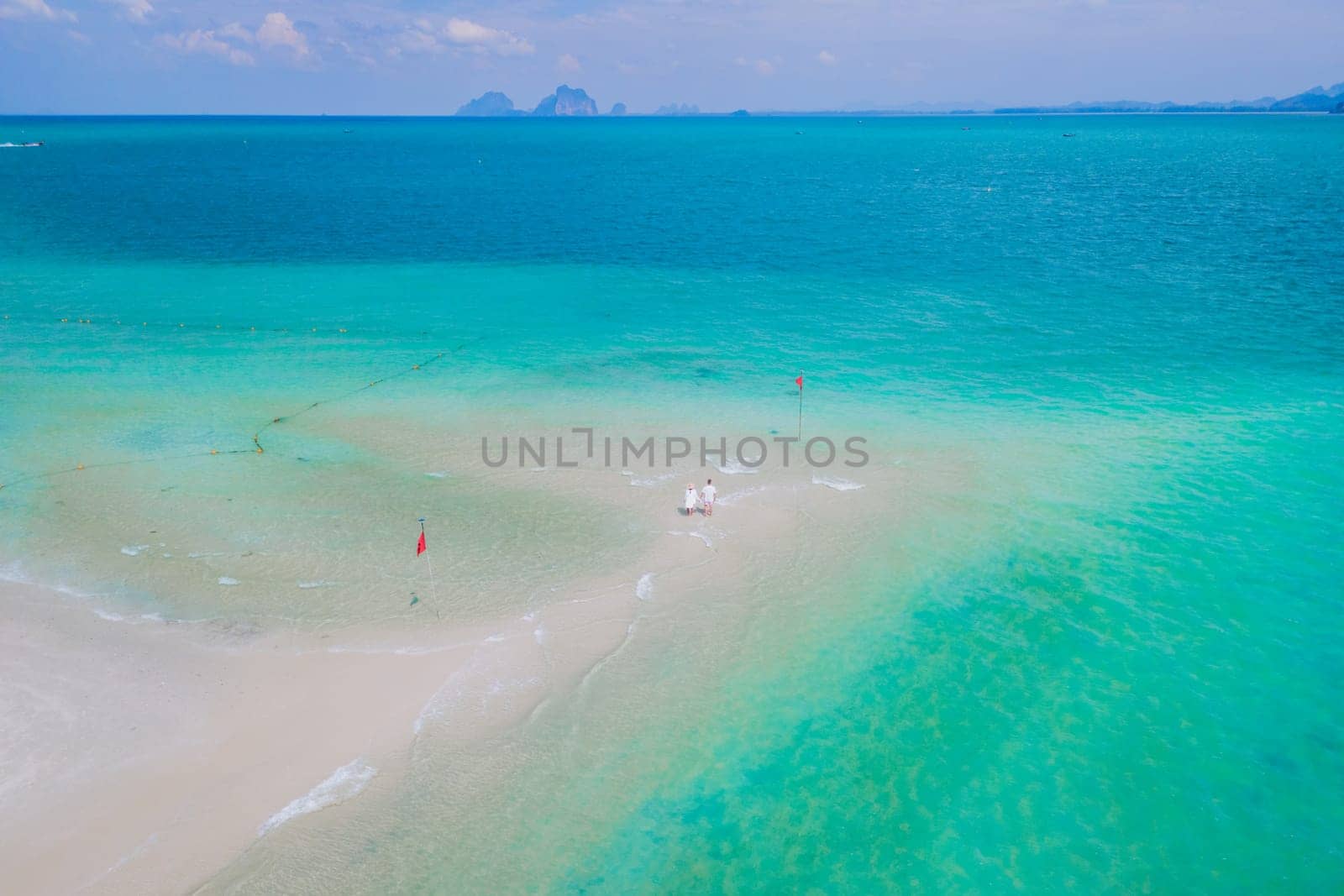 a couple of men and woman walking at a sandbar in the ocean of Koh Muk Thailand or Koh Mook by fokkebok